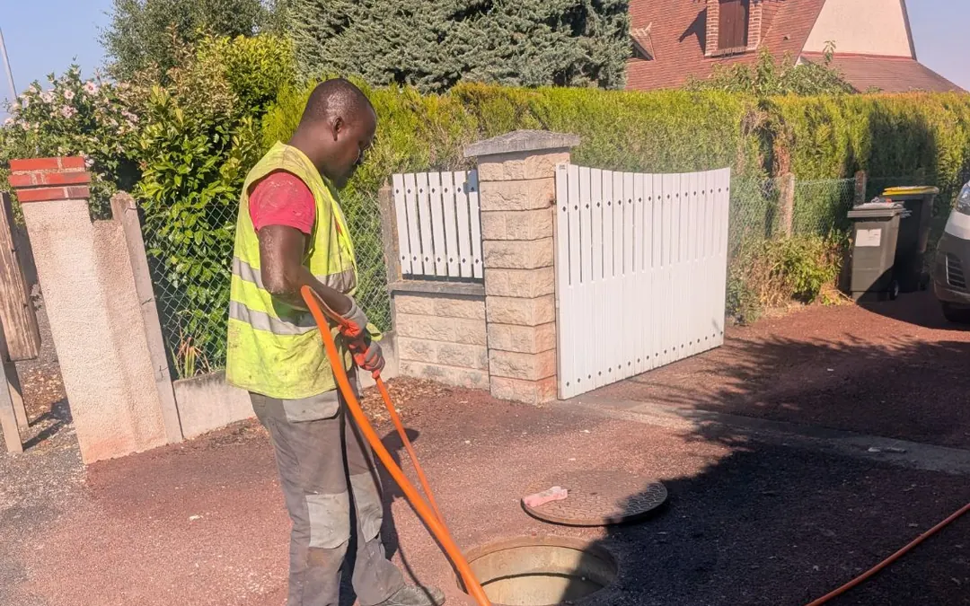 Technicien en gilet jaune avec un tuyau haute pression orange devant un regard d'assainissement ouvert
